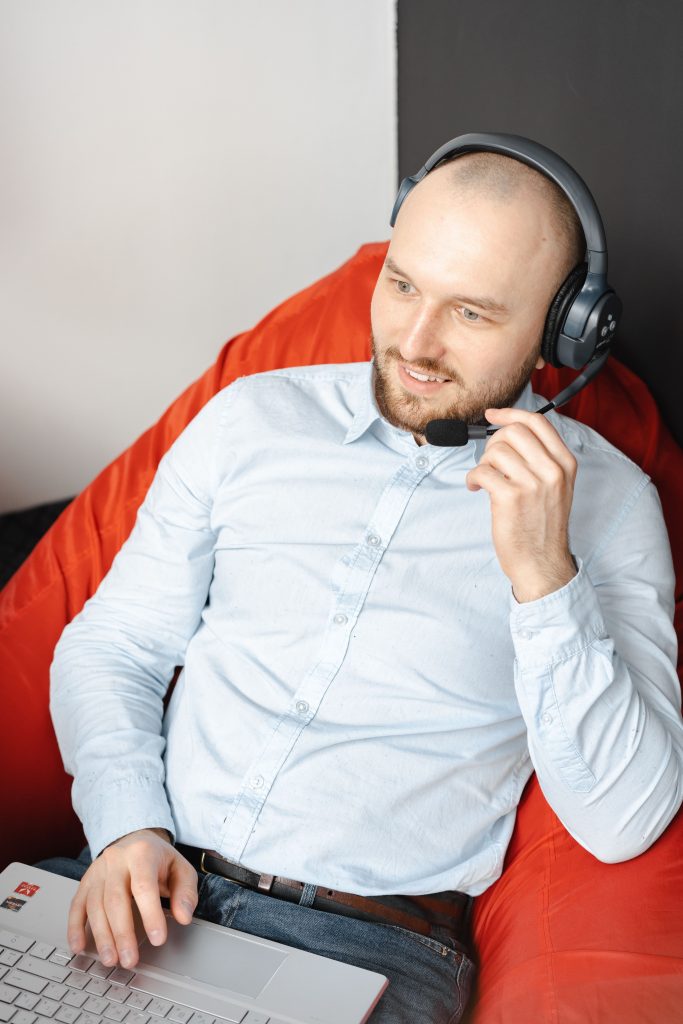 Professioneller Mann im blauen Hemd arbeitet mit Headset und Laptop im Homeoffice.