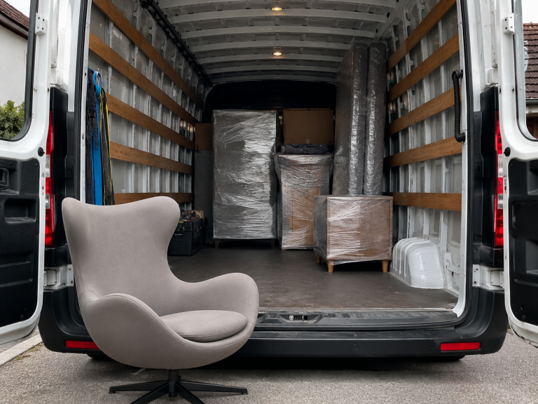 Das Bild zeigt einen beladenen Transporter mit einem Designer Sessel davor.